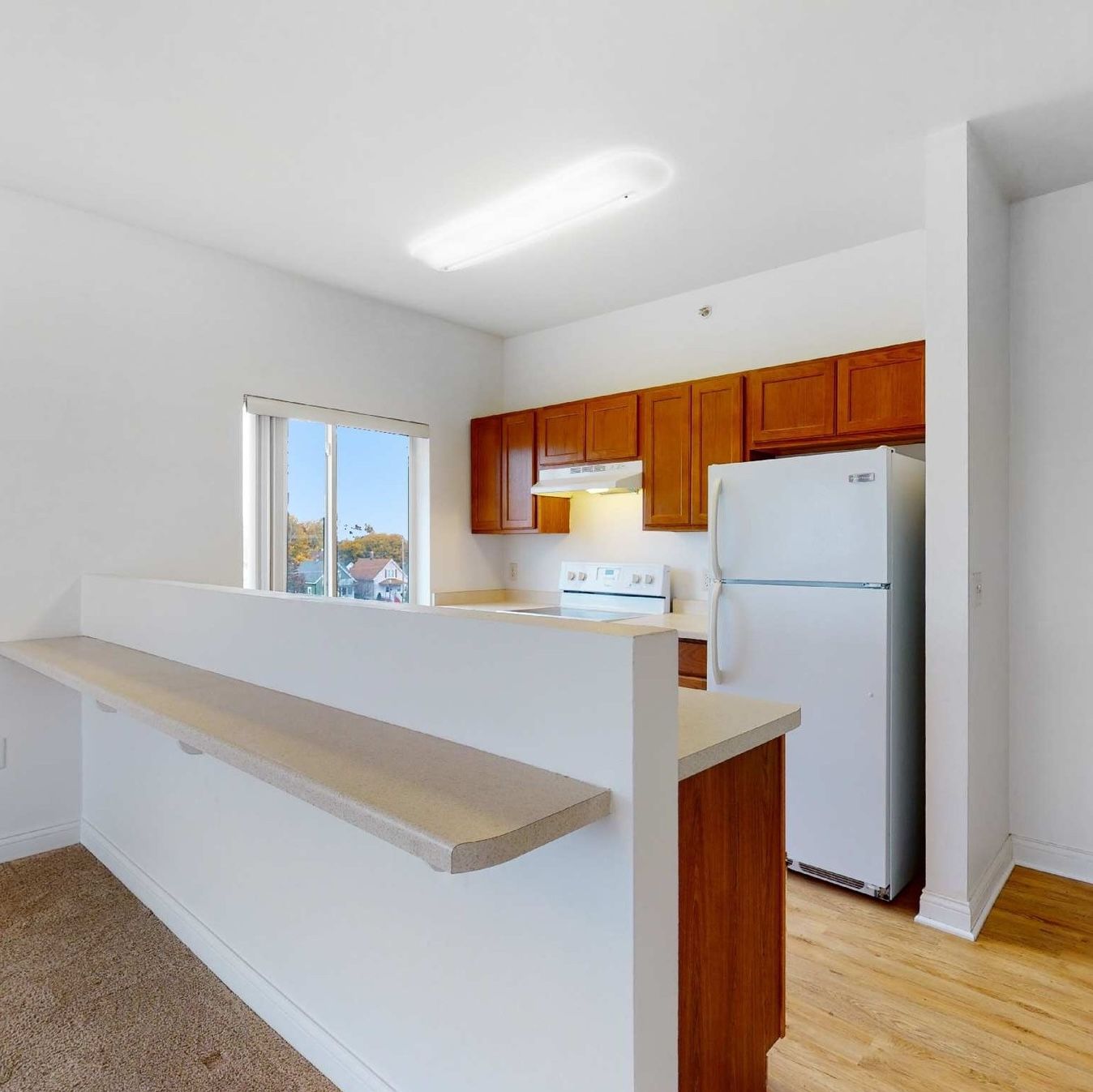 Uptown Brass Apartments A bright kitchen with wooden cabinets, a white refrigerator, and a double sink under a large window.